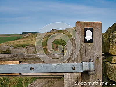 The white acorn National Trail sign on a weathered wooden gatepost shows the way of Hadrian`s Wall Path in the Northumberland Editorial Stock Photo