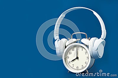 White alarm clock and headphones on a blue background. Music. Stock Photo