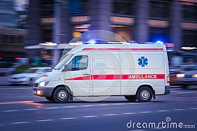 White Ambulance Van crosses a wide city street. Emergency vehicle with warning lights and siren moving fast on an avenue Stock Photo