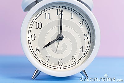White analog classic alarm clock with black arrows on a pink and light blue creative background Stock Photo
