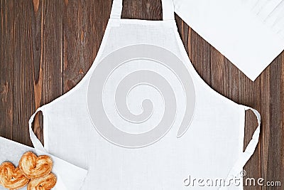 White apron template on brown wooden table with cookies, copy space. Kitchen, cooking clothing mockup Stock Photo