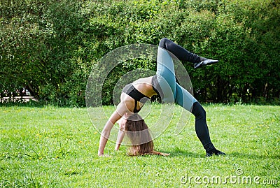 White athletic young woman in sportswear makes a bridge on the grass in the Park, yoga Stock Photo