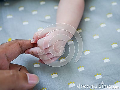White baby holding finger of black adult hand Stock Photo