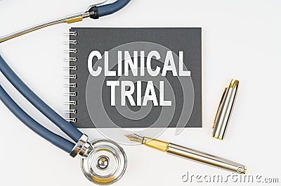 On a white background lie a stethoscope, a pen and a notebook with the inscription - CLINICAL TRIAL Stock Photo