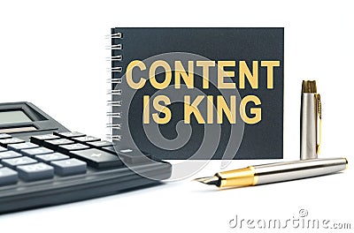 On a white background, there is a calculator, a pen and a black notebook with the inscription - CONTENT IS KING Stock Photo