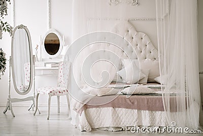 White bedroom interior with nobody. large cozy bed with a white canopy and oval dressing mirror with dressing table next Stock Photo