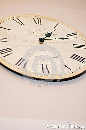 White and beige wooden wall clock with Roman numerals and black metallic hands, needles or pointers on a white wall. Old vintage Editorial Stock Photo