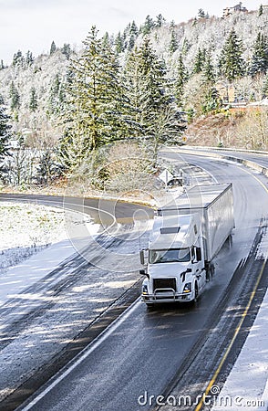 White big rig semi truck transporting cargo in semi trailer driving on winding winter snow road Stock Photo