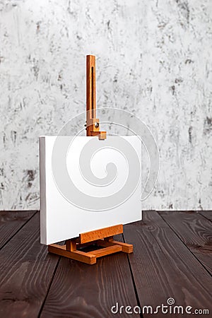White blank canvas stretched on subframe and an easel standing on a brown wooden table. Mockup Stock Photo