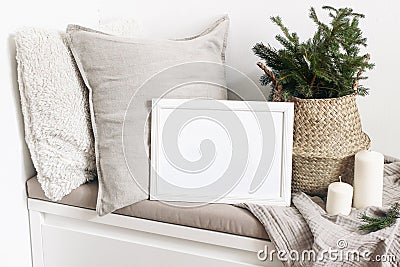 White blank wooden frame mockup with Christmas tree, candles, linen cushions and plaid on the white bench. Poster Stock Photo