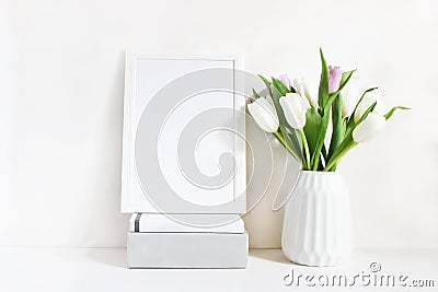 White blank wooden frame mockup with spring bouquet of tulips in porcelain vase and pile of books lying on the table Stock Photo