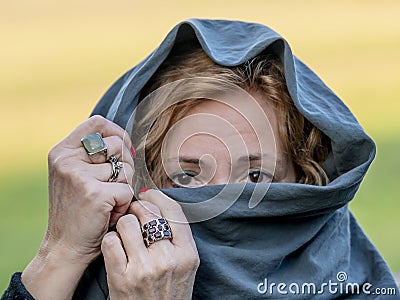 A white blonde woman has colorful rings adorning her hands while covering her head with a green scarf Stock Photo