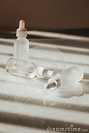 White and blue face serum and face oil bottles with droppers on white reflective tavle with water drops and light and shadow Stock Photo