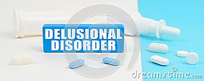 On a white and blue surface are pills, a spray and a wooden sign with the inscription - Delusional Disorder Stock Photo