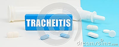 On a white and blue surface are pills, a spray and a wooden sign with the inscription - Tracheitis Stock Photo
