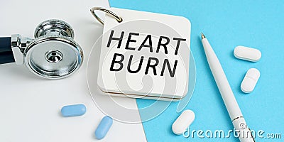 On a white and blue surface are pills, a stethoscope, a pen and a notepad with the inscription - HEART BURN Stock Photo