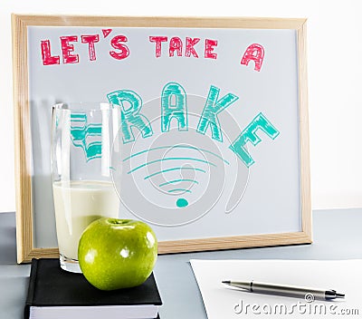 A white board title `let`s take a brake` red and green letters, school brake, cup of milk and green apple. Stock Photo