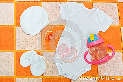 White bodysuit, Romper , white cap, white booties, the pacifier and teether. Things for babies in checked blanket Stock Photo