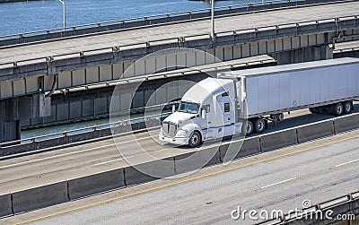 White bonnet big rig semi truck tractor transporting cargo in refrigerated semi trailer running on the multilevel overpass road Stock Photo