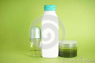 White bottle of shampoo, body scrub and deodorant on a green background Stock Photo