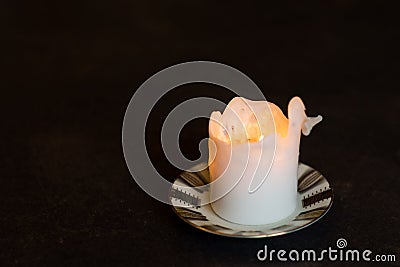 White burning pillar candle standing on gold decorated saucer on dark dining table Stock Photo