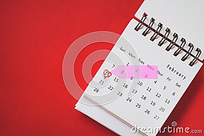 Calendar marked on 14 February with sweet pink arrow and red heart shape around date on grunge red paper background Stock Photo