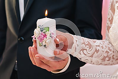 White candle with a decoration of flowers in the hands of the newlyweds. The concept of the family hearth Stock Photo