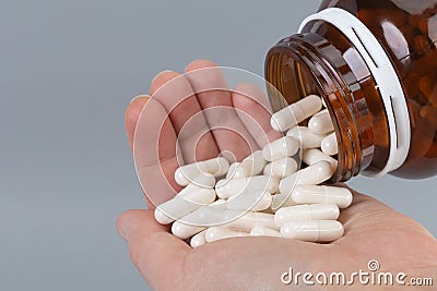 White capsules in the palm of a hand.Large amount of medicine.A hand with medicial pills on grey background.Healthcare, medicine Stock Photo
