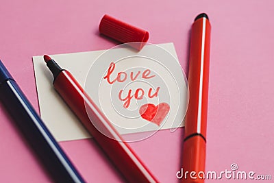 White card with the word `love you` and colored markers on a pink background Stock Photo