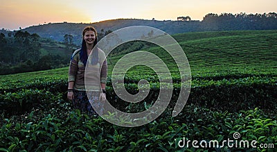 A white Caucasian young smiling woman with blue pigtails stands at sunset on a field with flowering bushes of tea. Stock Photo