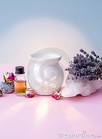 White ceramic candle aroma oil lamp with essential oil bottle and dried flowers, crystal geodes on modern pastel pink and blue bac Stock Photo