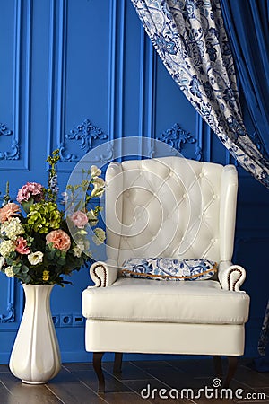 White chair a vase of flowers in the room with blue walls Stock Photo