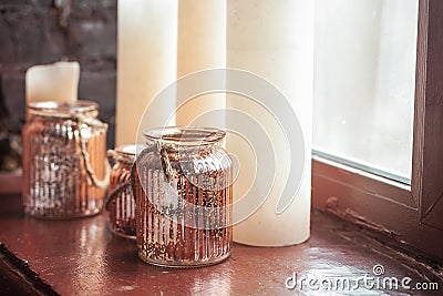 White Christmas candles and a glass jar with rustic twine standing onwindow sill Stock Photo