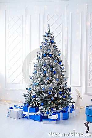 White christmas tree on white, decorated with blue ornaments and garland, lots of presents under the tree Stock Photo