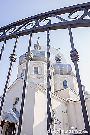 White church through iron fence. Ortodox cathedral on clear blue sky background. Religious architecture. Faith and pray concept. Stock Photo