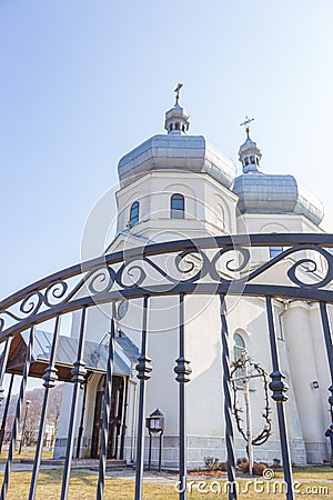White church through iron fence. Ortodox cathedral on clear blue sky background. Religious architecture. Faith and pray concept. Stock Photo