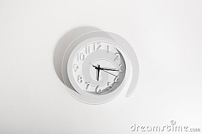 White classic circle clock with black arrows on white wall. Hard light Stock Photo