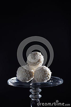 white coconut balls of candy on a glass luxury stand on a black background, exquisite dessert, heavenly delight Stock Photo