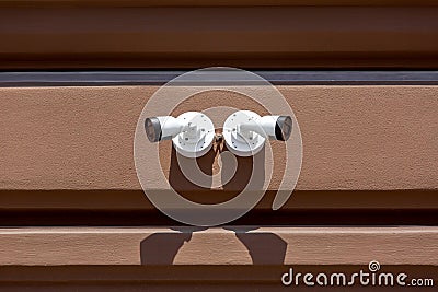 2 White color CCTV cameras fixed on the facade of a brown building. Stock Photo