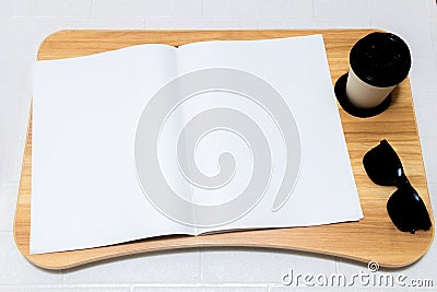 A white colored opened magazine laying out on the top of a table with wooden texture with a paper cup close Stock Photo