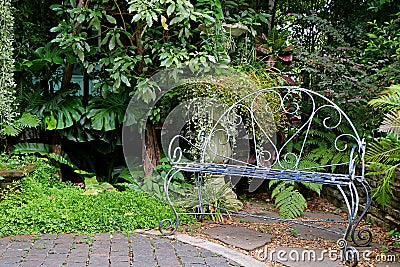 White colored wrought iron bench in the garden with tropical plants Stock Photo