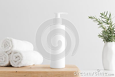 White cosmetic shampoo dispenser bottle mockup with towels and a rosemary on a wooden table Stock Photo