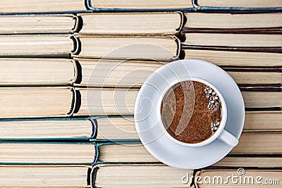 A white cup of aromatic coffee against the background of worn out old books folded upside down Stock Photo