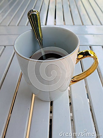 A white cup of coffee with a golden handle and a teaspoon in it Stock Photo