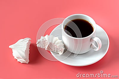 A white cup with coffee on a saucer and a white vanilla marshmallow broken into two halves on a pink background Stock Photo