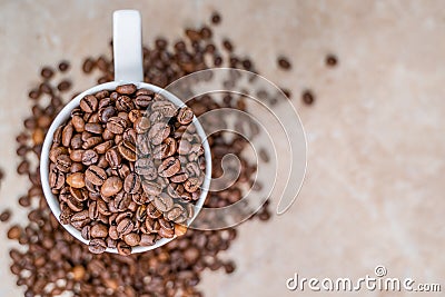 A white cup filled with roasted cinnamon coffee beans standing on brown marble surrounded by coffee beans Stock Photo