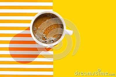 White cup of freshly brewed coffee with foamy crema on duotone yellow white striped background. Top view. Morning breakfast energy Stock Photo