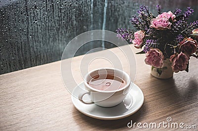 A white cup of lemon green tea on wooden table with drop water in rain season. cafe shop with rose flower in pot Stock Photo