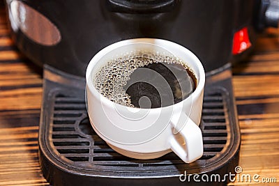 A white cup with prepared black coffee is in the coffee machine. Breakfasts and business meetings. Close-up Stock Photo