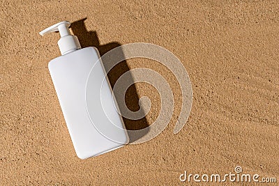 White dispenser with black hard shadow on the sand. Place for text. Stock Photo